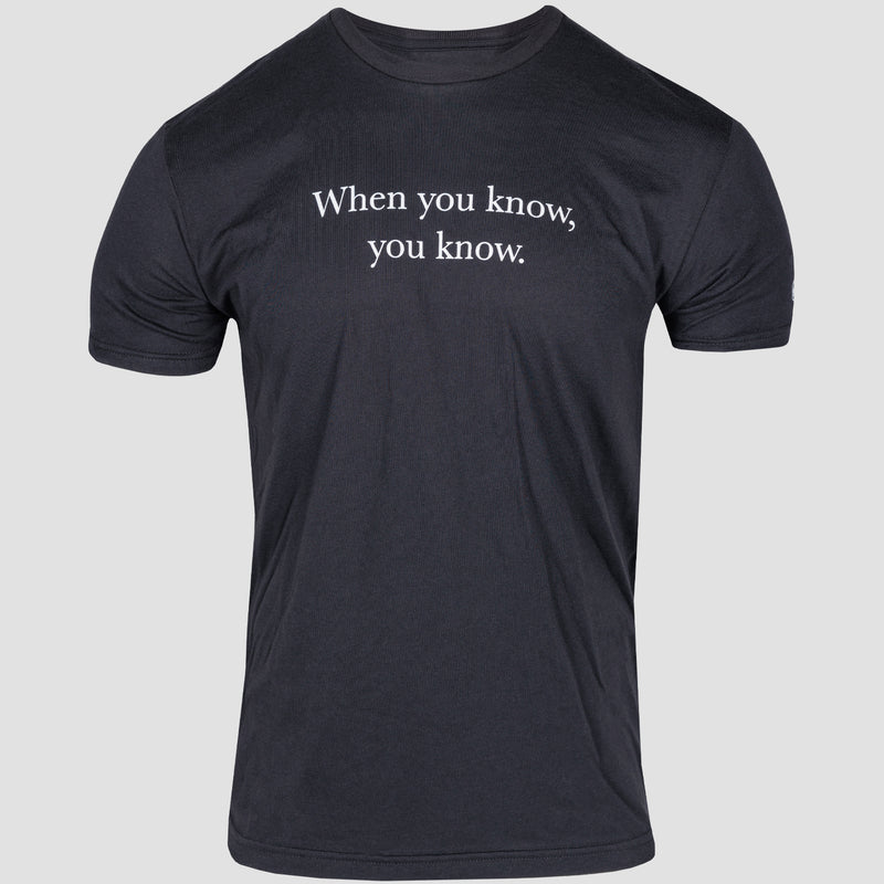 front view of black tee with "when you know, you know" printed on upper chest in white. mensa logo on left sleeve